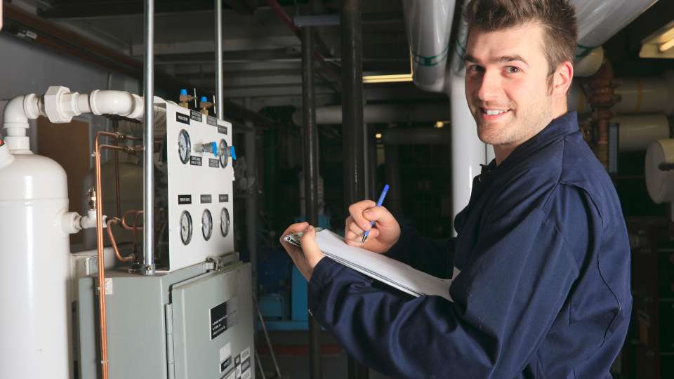 A male technician, acting as the data gatherer for his research dream team, smiles while documenting machinery readings on a clipboard.