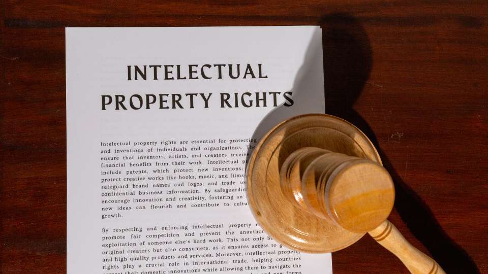 A high-angle photograph showing a wooden judge's gavel resting on a white document titled "Intellectual Property Rights" in bold black text. The document explains the importance of protecting inventions and creative works, reflecting the article's advice to establish a formal "Academic Prenup" or legal agreement between research partners to define ownership and access rights before a project begins. The scene is set on a dark wooden desk with dramatic lighting, symbolizing the serious legal expectations involved in global research collaborations.