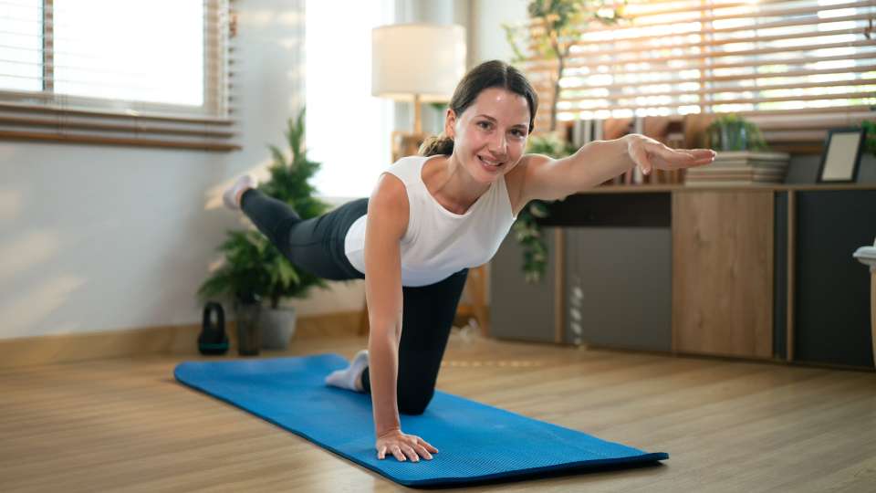 A woman performs a bird-dog extension on a yoga mat, extending her opposite arm and leg. This exercise is an effective way to strengthen the core and mitigate researcher back pain during long periods of home-based study and research.