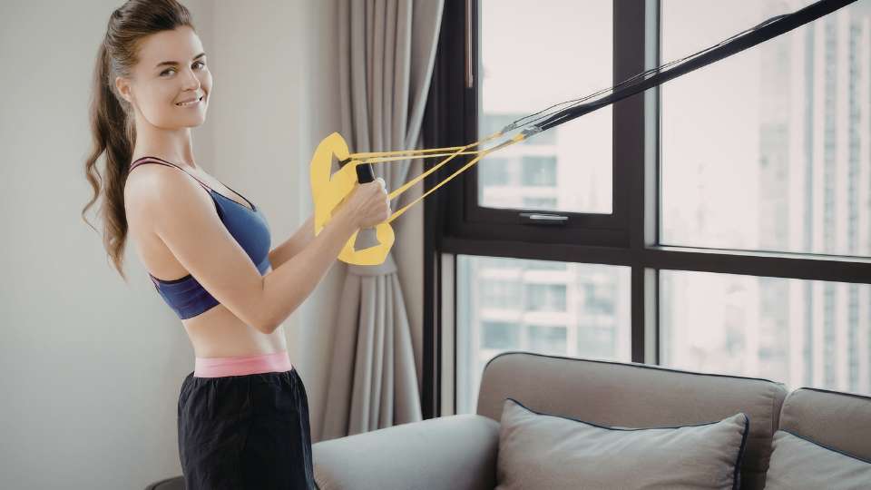 A woman smiles while using resistance bands attached to a door anchor in a hotel room. This versatile travel workout gear demonstrates how researchers can stay active on the go and integrate a full-body workout into their busy academic career travel schedules.