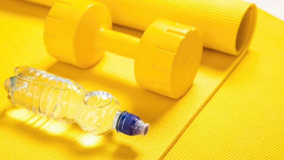 A yellow dumbbell, water bottle, and rolled-up mat. This setup represents portable home workout equipment for busy researchers, illustrating how to maintain a fitness routine while traveling for an academic career.