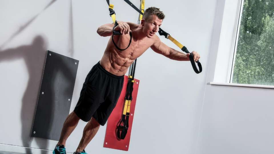 A man performs a chest press using suspension trainer straps anchored to a wall. This versatile travel workout gear is an ideal solution for researchers looking to maintain a high level of physical fitness in their hotel rooms while on the go for international conferences.