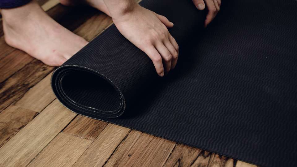 Hands rolling out a black mat on a wooden floor. This portable travel workout gear allows researchers to maintain physical health and mental clarity while on the go.
