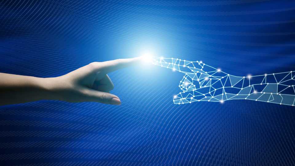 A human hand and a digital, geometric wireframe hand point toward each other, their index fingers nearly touching at a bright glowing light source against a blue mesh background, symbolizing the integration of modern AI technology into human workflows.
