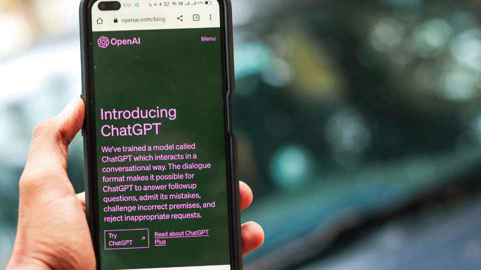 A person holds a smartphone displaying the OpenAI blog page titled "Introducing ChatGPT," which explains the conversational nature of the AI model.