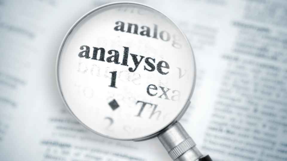 A close-up view through a magnifying glass focused on the word "analyse" printed in a dictionary, surrounded by blurred adjacent words like "analog" and "exa".